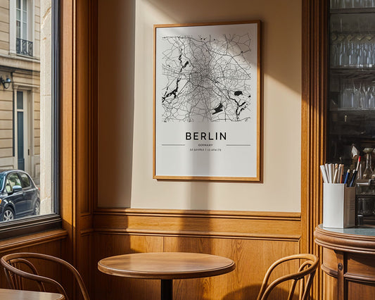 An FN Prints Berlin City Map decorates a wooden-paneled wall in a cozy café corner with two round wooden tables and chairs, where sunlight streaming through the windows creates a warm atmosphere.