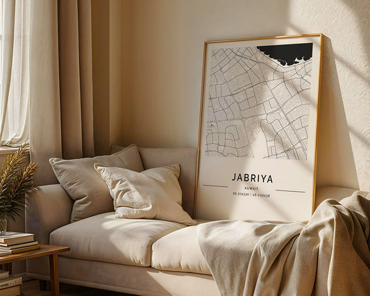 A cozy room showcases a beige sofa adorned with plush cushions and a blanket. The FN Prints Jabriya City Map elegantly rests on the sofa, while sunlight pours through a window, highlighting a stack of books and a plant on the side table.
