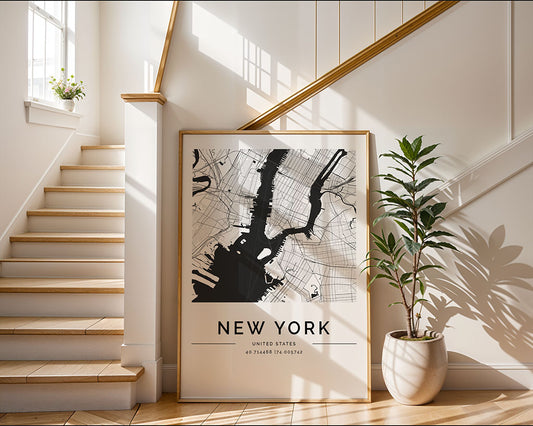 The FN Prints New York City Map, a black and white minimalist art piece, leans against the wall by a wooden staircase. Sunlight highlights its design on the neutral walls, while a potted plant to the right enhances the tranquil setting.