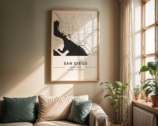 The FN Prints San Diego City Map hangs above a beige sofa with green and cream pillows. Sunlight from the window highlights several potted plants on the ledge, creating a calm, inviting atmosphere.