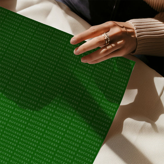 A person wearing a beige sweater and ring holds the FN Prints "Vince Lombardi - Winners Never Quit" green motivational art print featuring repeated white “SUCCESS,” while seated at a table with a white surface.