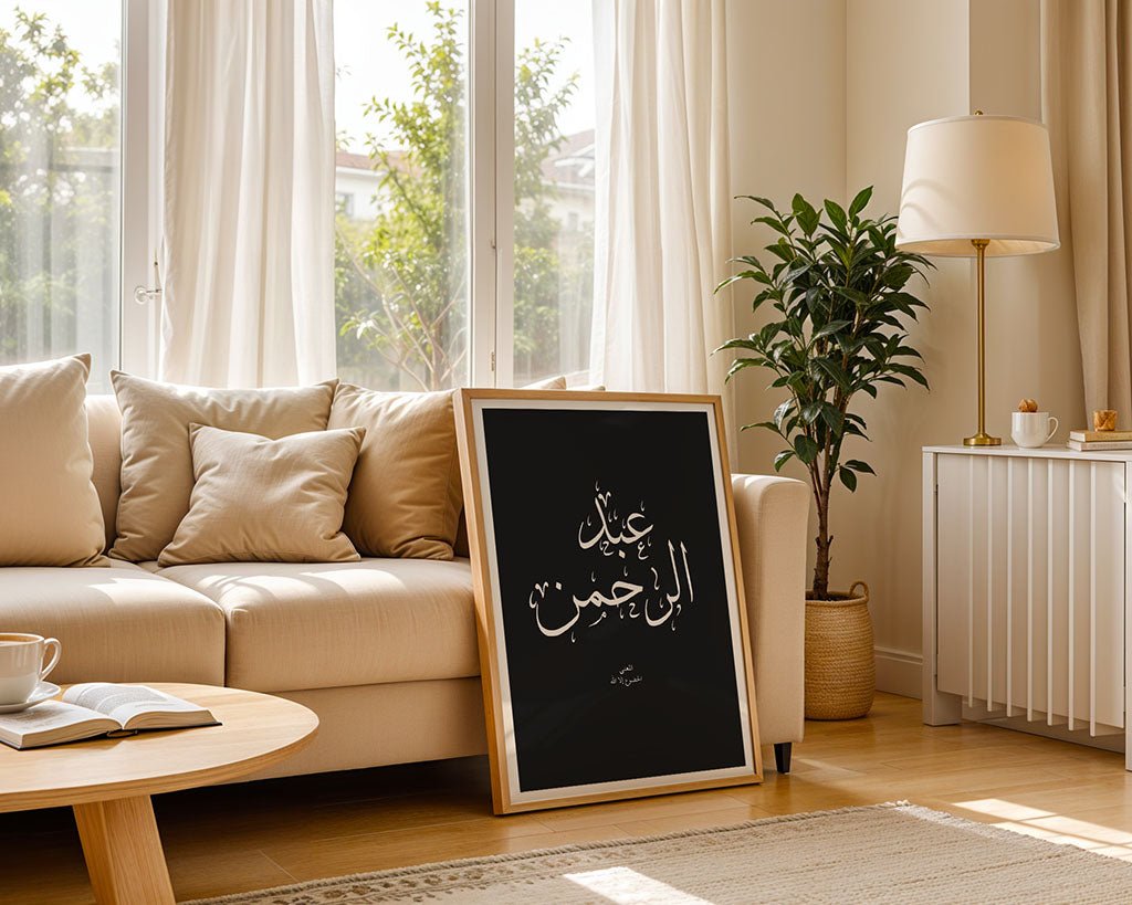 The Abdulrahman - عبدالرحمن Islamic wall art by FN Prints leans against a beige sofa in a bright living room featuring a large window, indoor plant, round coffee table, and cream-colored decor.