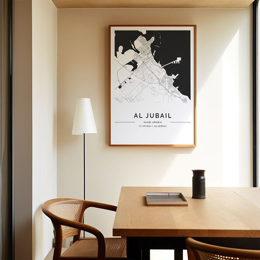 The FN Prints Al Jubail City Map hangs on a beige wall above a wooden table with a chair, book, and vase. A floor lamp is placed beside the table near the window.