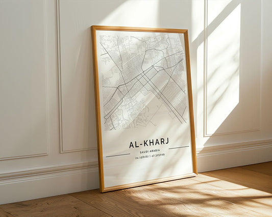 The FN Prints Al-Kharj City Map features a minimalist design, framed and leaning on a wooden floor against a white paneled wall. Sunlight highlights the detailed Saudi Arabia city coordinates and street outlines.