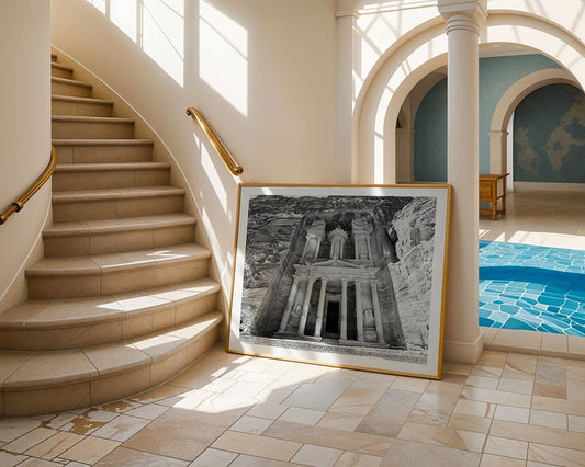 The FN Prints "Al-Khazneh - The Treasury - Petra: Part III" framed black and white photo rests against a curved staircase in a sunlit room with tiled floors, columns, and an indoor pool.
