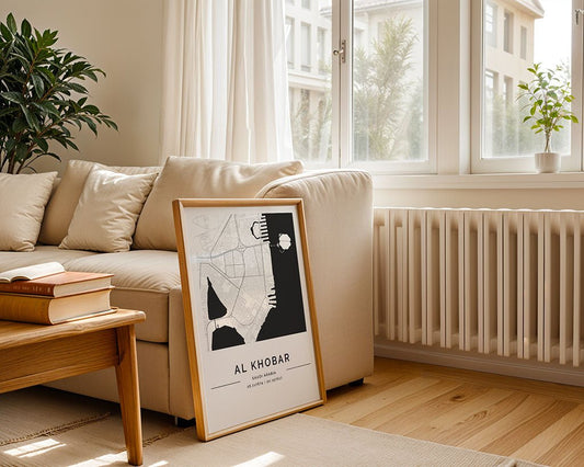 A framed FN Prints "Al Khobar City Map" rests against a beige sofa in a bright, minimalist living room with wooden floors and sunlight streaming in—a stylish nod to Saudi Arabia.