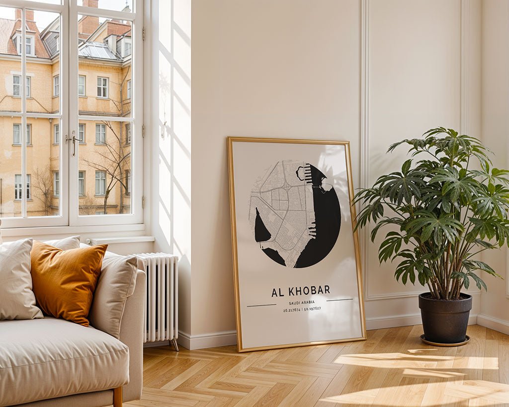 The FN Prints Al Khobar City Map, framed and labeled "Al Khobar," leans against a cream wall next to a green plant, bringing charm to a bright living room with minimalist décor and a beige sofa overlooking Saudi city views.