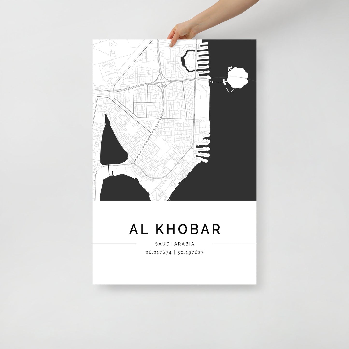 A hand holding a black and white map poster of Al Khobar city, with distinct areas marked in white on a black background.
