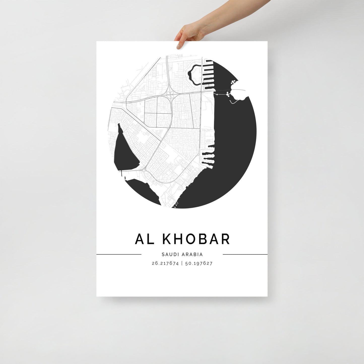 A hand holding a black and white map poster of Al Khobar city, with distinct areas marked in white on a black background.