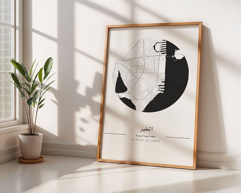 The FN Prints Al Khobar City Map, framed in black and white, leans against a white wall on a sunlit floor. A green potted plant adds freshness to the minimalist space as window shadows dance across the room.