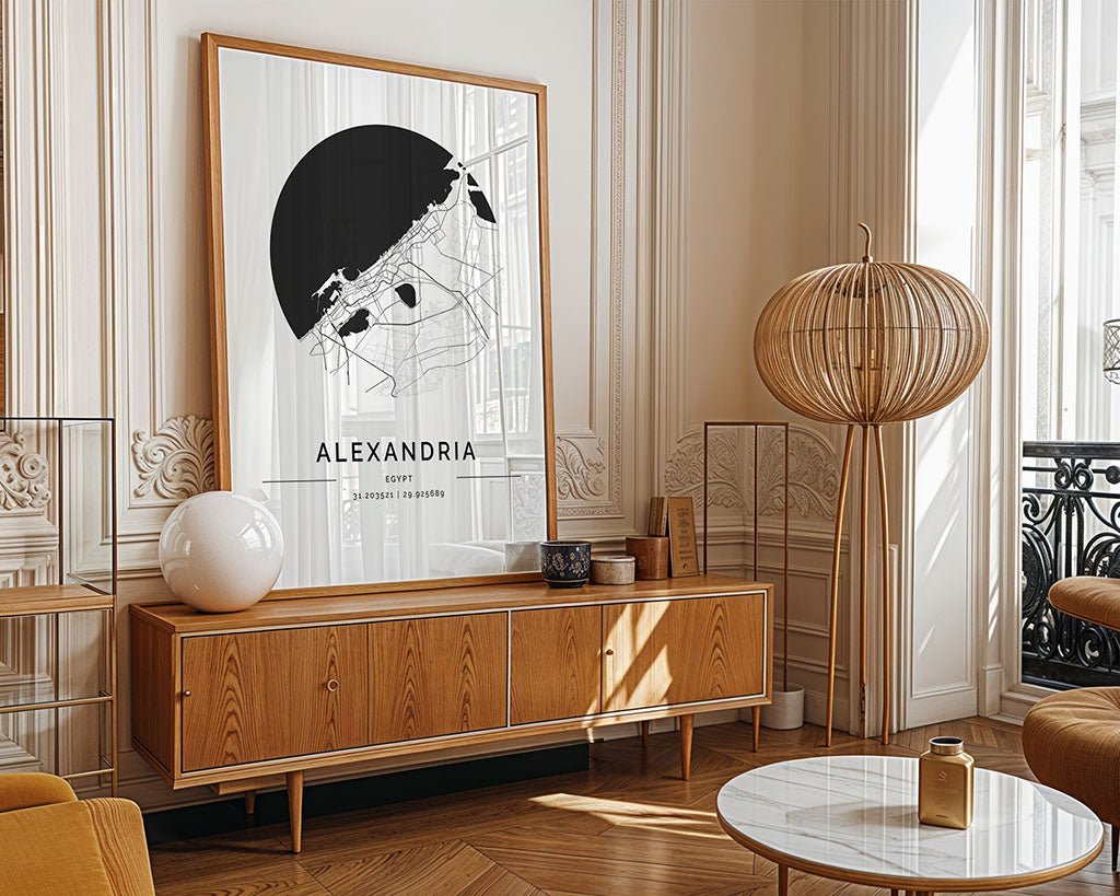 A stylish living room displays a wooden sideboard and the FN Prints' Alexandria City Map, a large black and white poster. A spherical rattan lamp and round white marble coffee table are illuminated by natural light from the windows, highlighting the elegant decor with ornate molding.