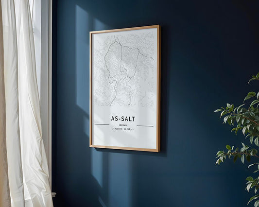 An FN Prints framed As-Salt City Map on museum-quality paper adorns a dark blue wall. Sunlight filters through cream curtains on the left, casting charming shadows. A leafy plant peeks into view on the right, blending nature with elegance in this scene.