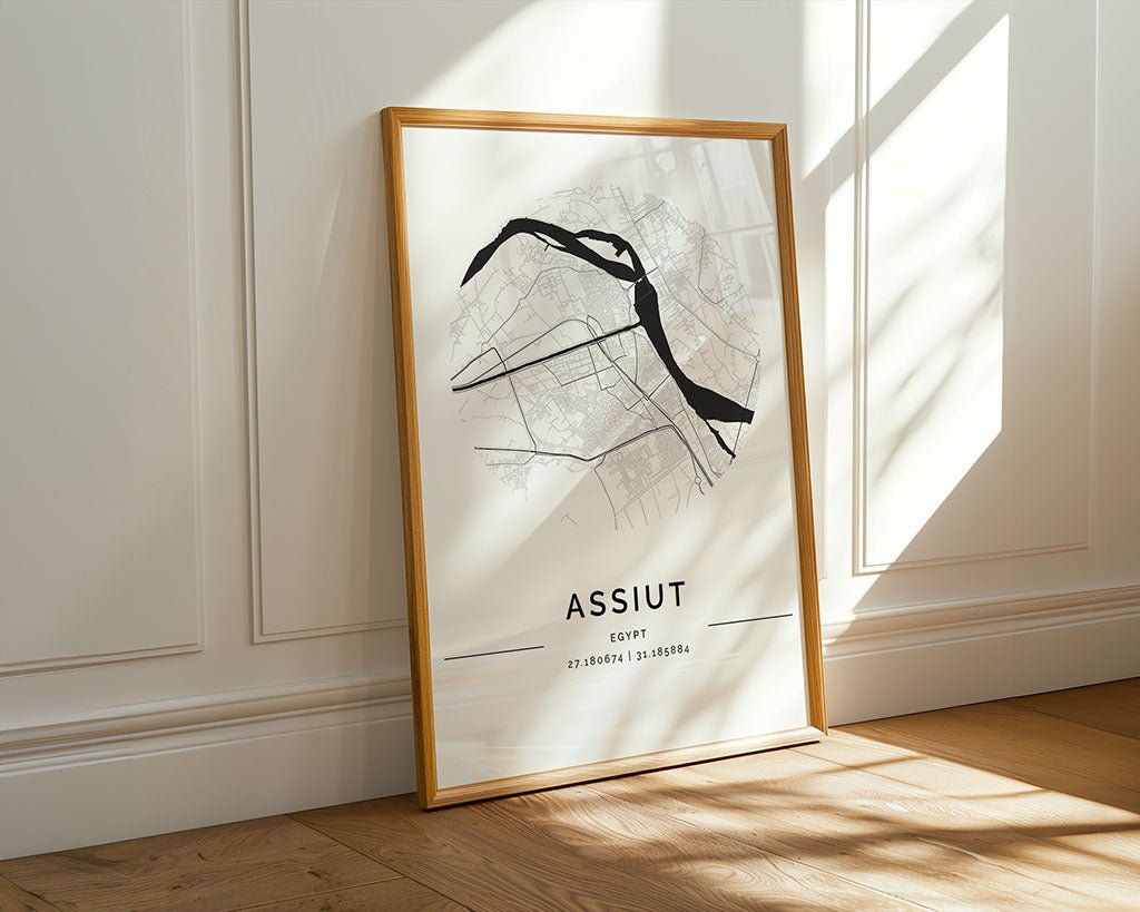 The Assiut City Map by FN Prints is a framed poster on museum-quality fine art paper. It rests against a white wall, showcasing minimalist black map lines on a white backdrop with coordinates below, as sunlight casts floor shadows.