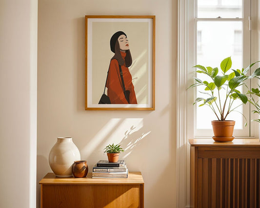 The framed "Autumn Muse" fashion illustration by FN Prints, featuring a woman in a red turtleneck and black hat, hangs above a wooden cabinet with ceramics and plants, adding chic minimalist style to the sunlit room.