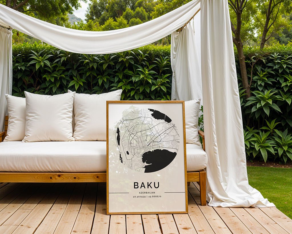 A wooden-framed Baku City Map by FN Prints, ideal for architecture enthusiasts, leans against a white outdoor daybed. Lush greenery serves as the backdrop. The daybed rests on a wooden deck with white draped canopy curtains adding elegance.