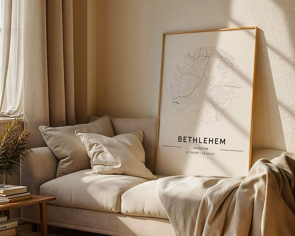 In the cozy living room, a beige sofa with cream pillows and a blanket stands out. The focal point is the large FN Prints' Bethlehem City Map on museum-quality paper leaning against the wall. Sunlight filters through sheer curtains, casting shadows on the light walls and floor.