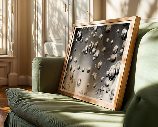 FN Prints' "Bubbles In Glass," a framed black-and-white abstract photograph, leans against a green upholstered sofa. Sunlight through the window casts artistic shadows, imbuing the room with sophistication and serenity.