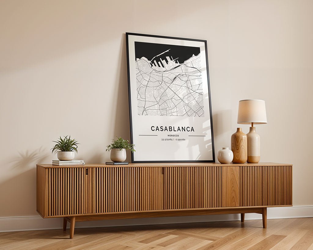 A wooden sideboard with ribbed design stands against a light wall, adorned with small potted plants, vases, and a table lamp. FN Prints' framed Casablanca City Map adds a minimalist print vibe. The chic setting, enhanced by the wooden floor, makes for an ideal housewarming gift for style lovers.