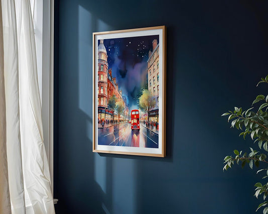 City Nights: Double Decker Bus" by FN Prints, a framed London wall art featuring a red double-decker bus on a city street, hangs on a dark blue wall with sunlight, white curtains, and a green plant in the corner.