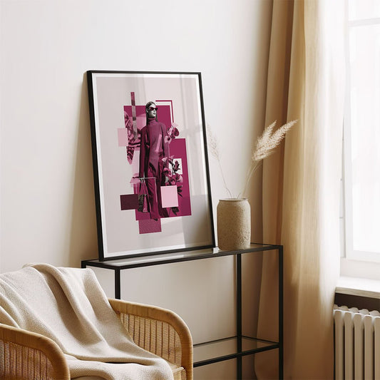 Crimson Poise by FN Prints, a framed abstract portrait with pink tones, stands on a black console next to a beige vase of dried grass. A wicker chair with a cream blanket and soft curtains complete the room’s modern, fashion-inspired look.