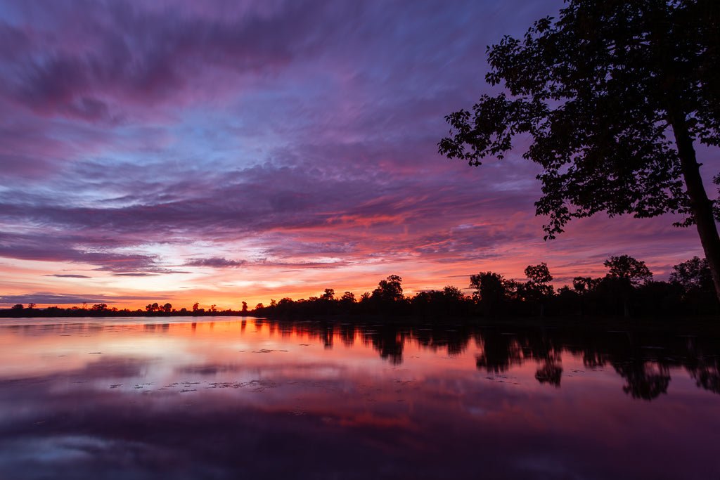 A lake in Cambodia during sunrise with orange, purple and yellow hues.