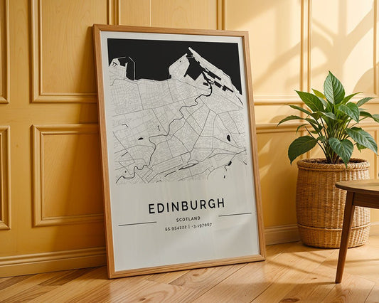 FN Prints' Edinburgh City Map, a framed minimalist print with geographical coordinates, leans against a wooden paneled wall. A potted plant in a wicker basket is on the wooden floor, and natural light highlights the museum-quality fine art paper.