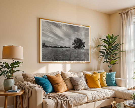 A bright living room featuring a beige sofa, colorful throw pillows, a floor lamp, potted plants, and FN Prints' "English Field Black & White" framed photograph hanging above the sofa.