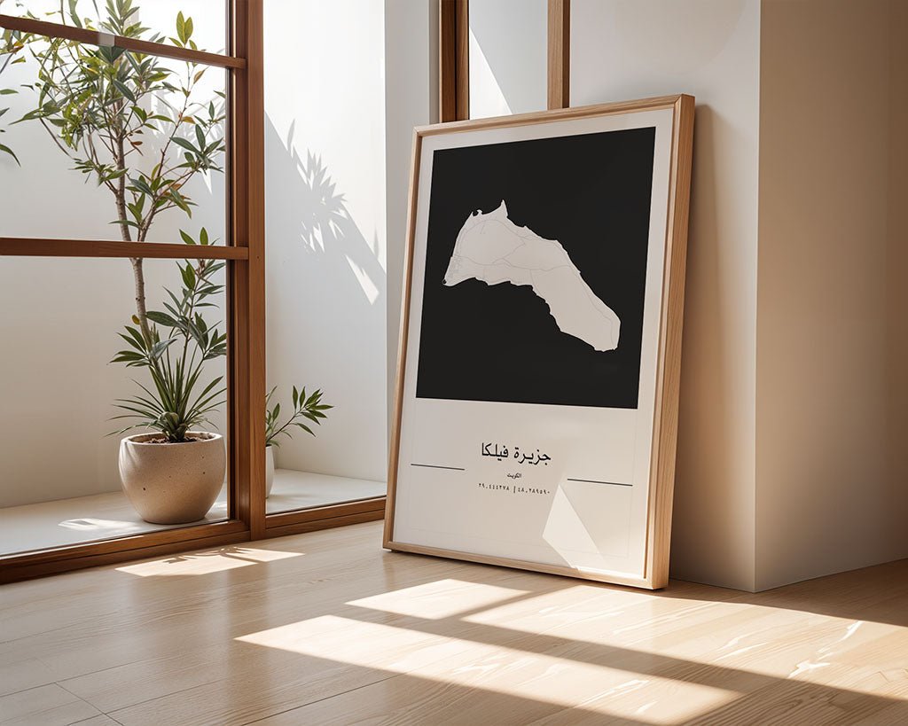 In a sunlit room, an FN Prints Failaka Island City Map is propped against a wall. Nearby, a potted plant enhances the scene as large windows bathe the space in natural light, creating an inviting atmosphere reminiscent of minimalist designs.