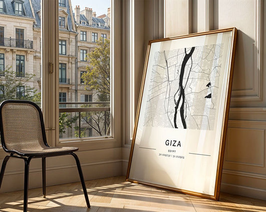 A FN Prints Giza City Map print leans against a sunlit wall, paired with a black chair. Through the window, classic stone buildings and trees contrast with the map's museum-quality fine art paper rendering.