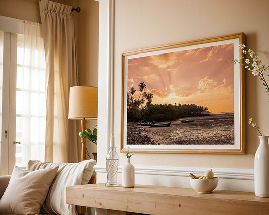 A living room with beige walls and light furniture features FN Prints' "Goan Beach Sunset"—a framed photograph of palm trees and boats—adding stunning coastal decor above a wooden console table.