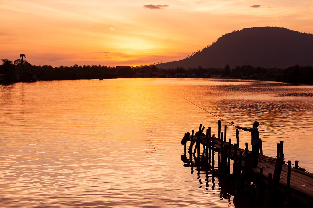 A man casting his fishing rod in to a lake in Cambodia during sunset.