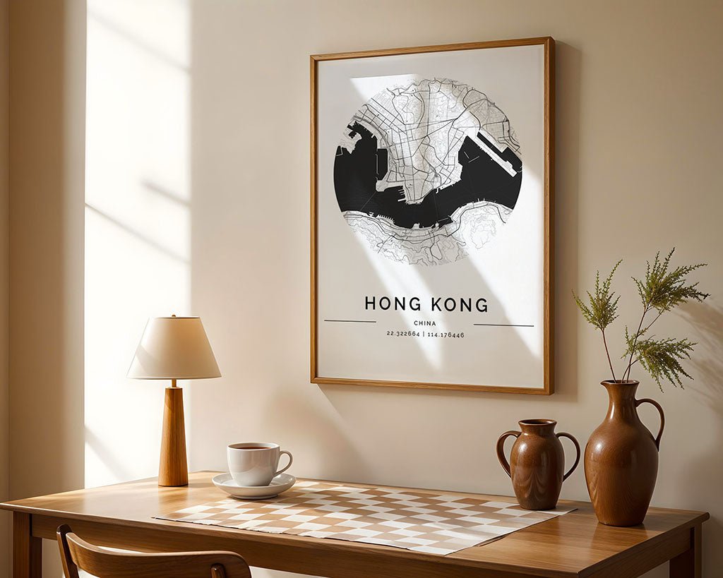 A room features a wooden table with two brown vases, a lamp, and a cup. On the beige wall above hangs FN Prints' elegant Hong Kong City Map framed as a minimalist print. Sunlight filters through the window, casting warm shadows and enhancing the serene home décor atmosphere.