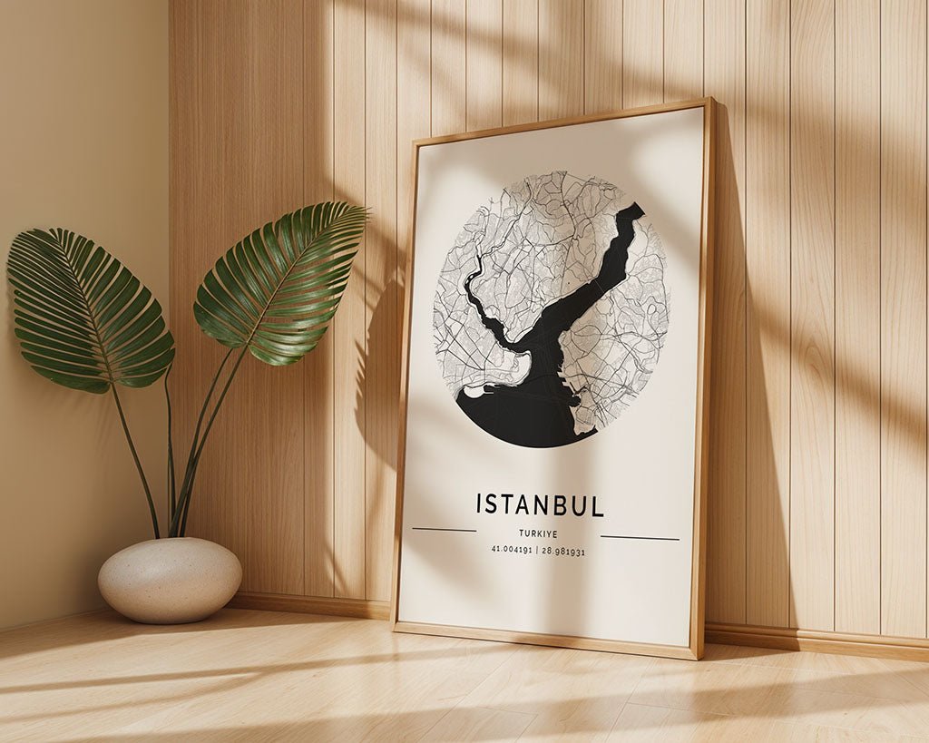 FN Prints' Istanbul City Map, a framed black and white minimalist poster, leans against a wooden wall with sunlight casting playful shadows. A decorative plant in a white pot enhances the scene, beautifully capturing Istanbul's urban design essence.
