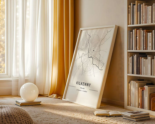 A cozy room has a floor-to-ceiling window with yellow curtains. A minimalist Kilkenny City Map by FN Prints, crafted on museum-quality fine art paper, leans on a stack of books. On the rug, a round white lamp glows next to a filled bookshelf on the right.