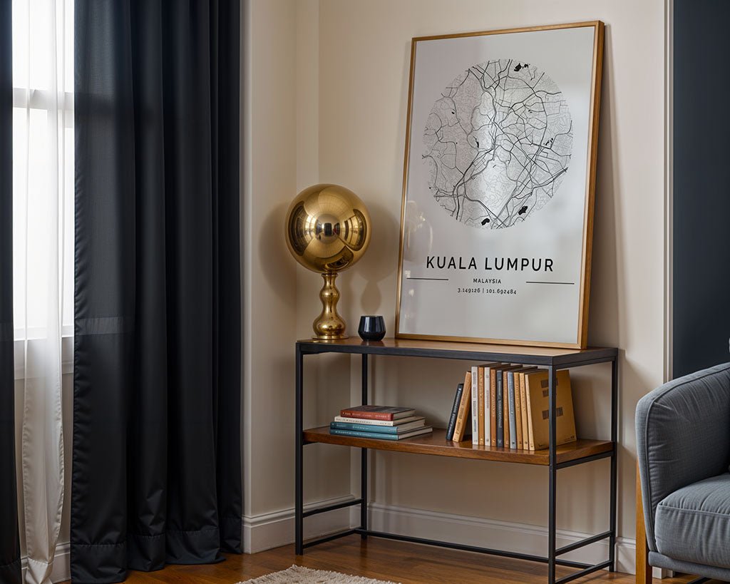 A minimalist room corner showcases an urban vibe with FN Prints' large Kuala Lumpur City Map in a wooden frame against the wall. A gold spherical lamp and small books rest on a wooden shelf below, while dark curtains and a gray sofa add to the sleek atmosphere.