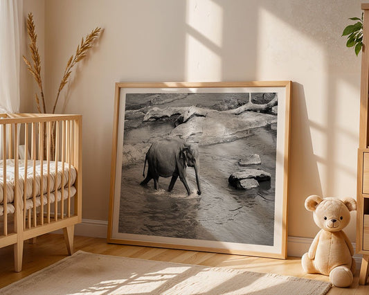 The Lone Elephant framed art print by FN Prints, inspired by a Wilpattu National Park photo, rests against a wall in a softly lit nursery with a crib, dried grass in a vase, and a plush teddy bear on the wooden floor.