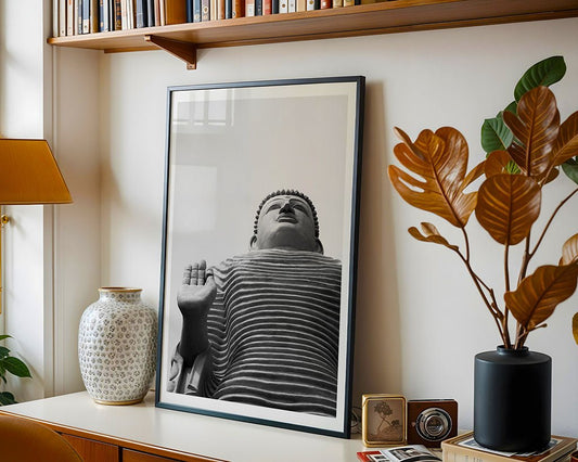 The FN Prints "Lord Buddha: Tsunami Honganji Viharaya" framed black-and-white photo sits on a desk with a ceramic vase, potted plant, and vintage camera, beneath shelves filled with books.