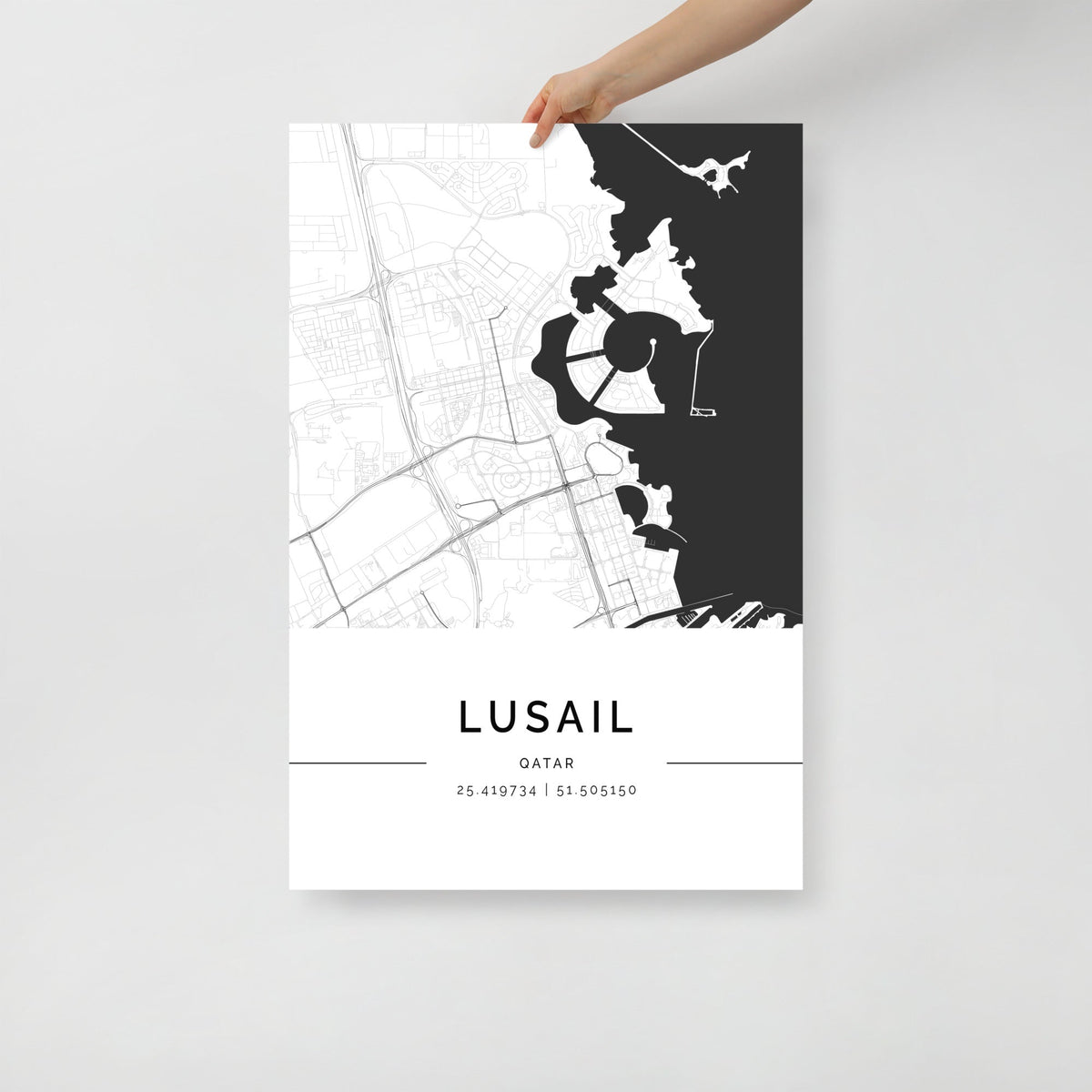 A black and white minimalist map poster of Lusail City, Qatar, held by a hand against a white background.