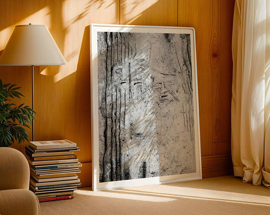 The framed "Mount Nebo Monolith: Jordan" black and white print by FN Prints rests on the floor against a wood-paneled wall, beside a book stack, beige armchair, potted plant, and lamp, with sunlight streaming in through the window.