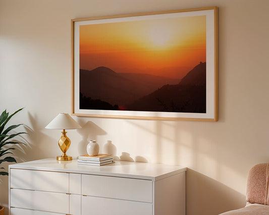 A white dresser with a lamp, books, and vases sits against the wall. Above it hangs “Mountain Sunset” by FN Prints—a large framed wall art featuring a vivid mountain landscape with an orange and yellow sky.