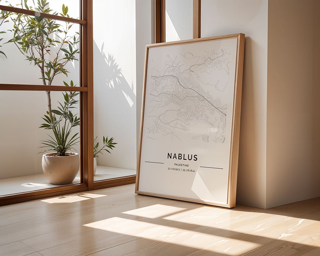 A museum-quality FN Prints Nablus City Map leans against a wall on a wooden floor, bathed in sunlight. A nearby potted plant enjoys the natural light streaming through the window, casting elegant shadows on this city wall art.
