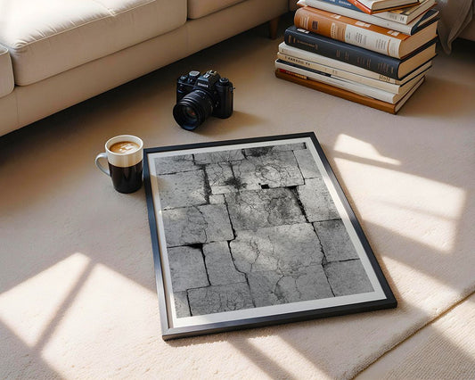 The framed "Nature Finds A Way" photo by FN Prints, featuring cracked Jordanian sandstone, rests on a beige carpet beside coffee, a camera, and books—an elegant accent for sunlit, nature-inspired living rooms.