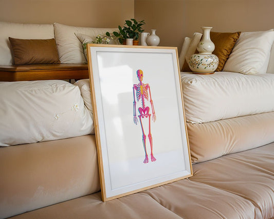 The Neon Skeleton by FN Prints, a framed anatomical artwork with colorful highlights, leans against a beige sofa accented by decorative pillows and vases, creating a vibrant modern pop art print display.