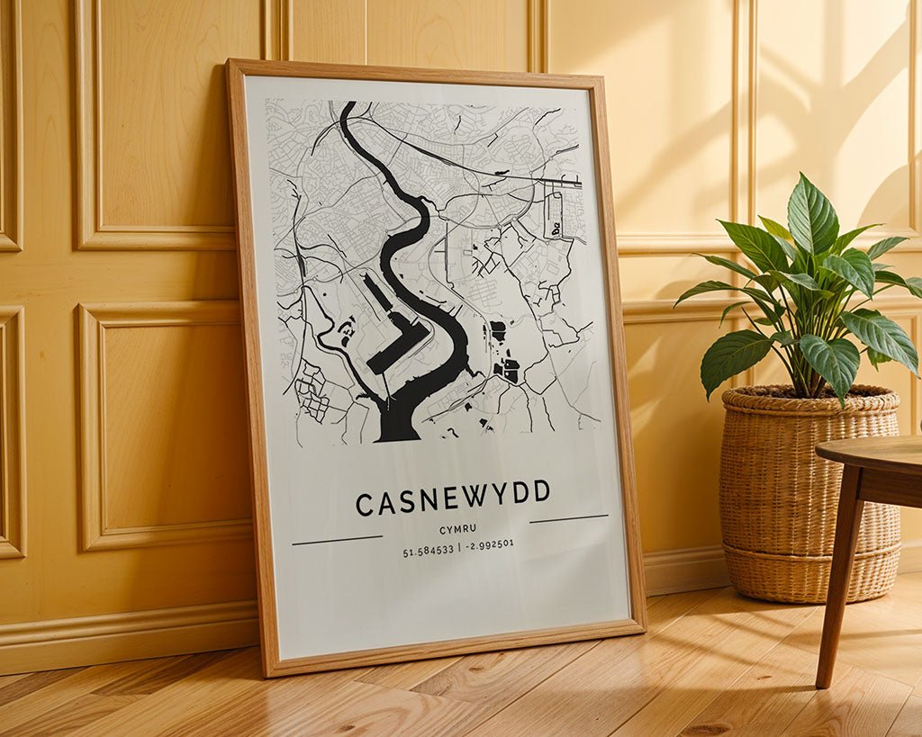 A framed FN Prints Newport City Map with coordinates 51.584953° N, 2.993090° W leans against a yellow paneled wall, next to a woven basket with a green plant on the floor, creating a minimalist vibe ideal for fine art lovers.
