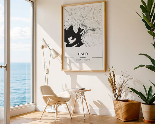 A minimalistic room with Scandinavian style displays a large FN Prints Oslo City Map on the wall. The space includes a chair, small side table with a book, floor lamp, and potted plants. Large windows provide an ocean view beneath a clear sky.