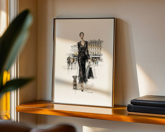 The framed "Parisian Glam" fashion illustration by FN Prints shows a woman in a black dress walking her dog. It sits on a wooden shelf beside two closed books, with sunlight partially illuminating this chic Parisian wall decor.