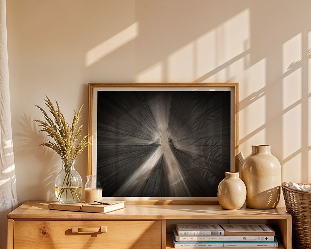 The wooden sideboard displays FN Prints' "Pedestrian Crossing Person" framed artwork in neutral tones alongside a striking black and white photograph. Beige ceramic vases, a glass bottle with dried plants, and sunlight patterns on the wall complete the scene, with stacked books nearby.