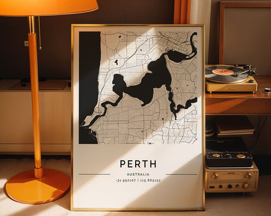 A framed Perth City Map by FN Prints is elegantly positioned on the floor next to a vintage record player, under a tall orange lamp. This minimalist black and white print with coordinates leans against the wall, adding understated elegance to any modern interior.