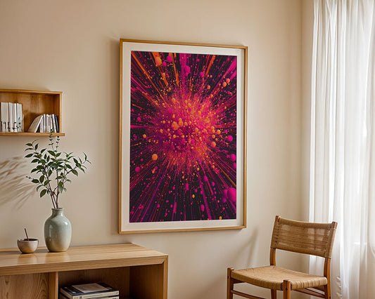 A framed digital artwork titled "Pink Orange Explosion" by FN Prints showcases a vibrant burst of pink and orange abstract forms, adorning a beige wall. Nearby, there is a simple chair and a small table with a vase and plant. Gentle sunlight streams through a sheer curtain on the right.
