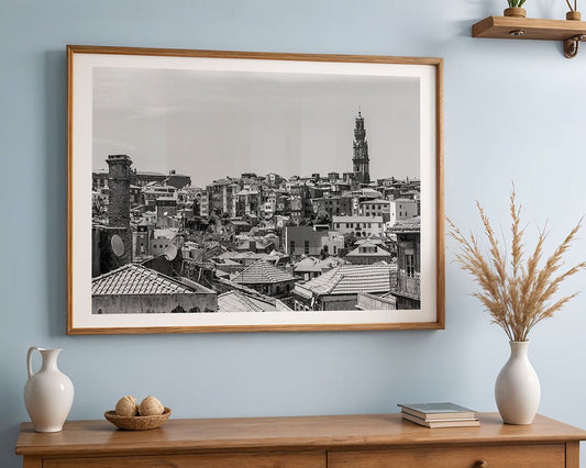 The "Porto Rooftops" black and white cityscape by FN Prints is displayed in a wooden frame on a light blue wall above a wooden console table decorated with vases, woven balls, books, and dried grass.
